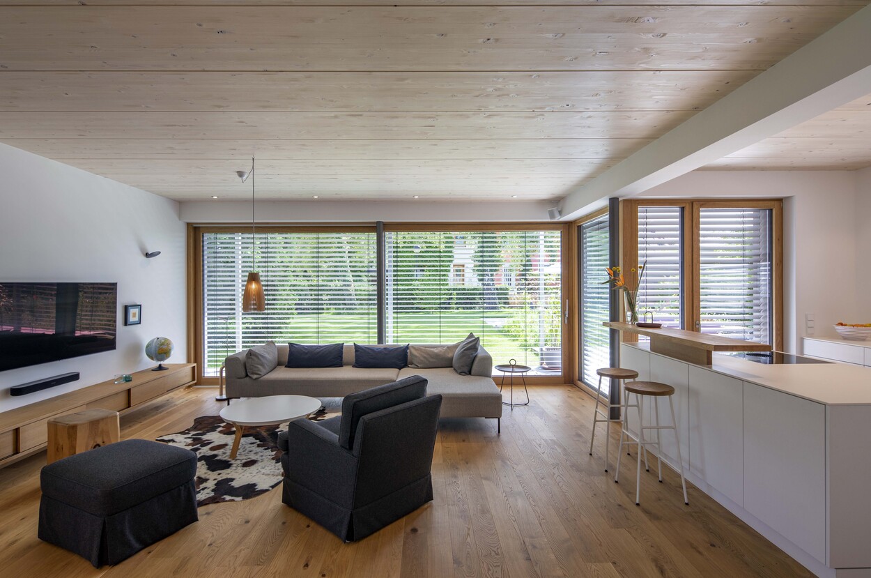 Ein modernes Wohnzimmer in Gröbenzell zeigt stilvolle Einrichtung, Holzboden und große Fenster mit Gartenblick.