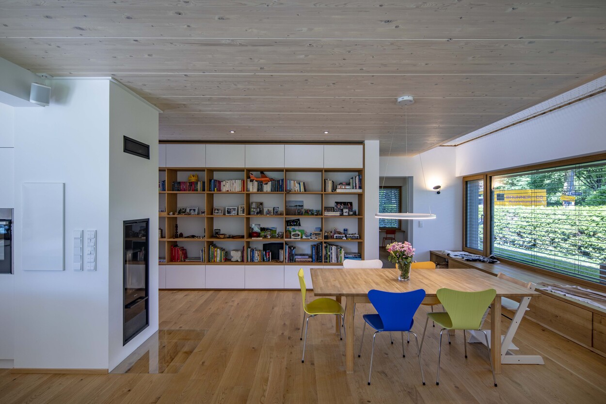 Ein modernes Holzhaus in Gröbenzell bietet ein einladendes Esszimmer mit bunten Stühlen und einem großen Bücherregal.