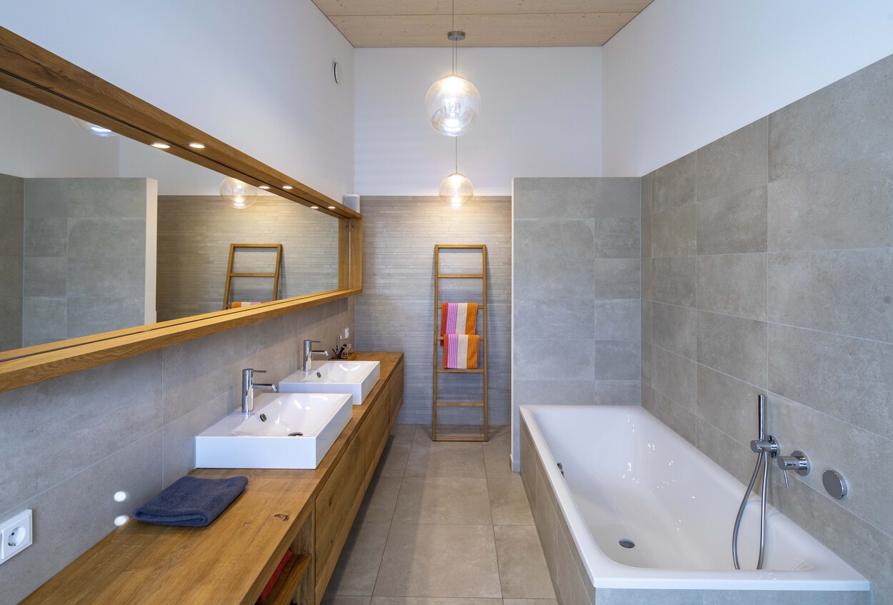 Modernes Badezimmer in einem Holzhaus in Gröbenzell mit Doppelwaschbecken, Badewanne und einem stilvollen Handtuchhalter.