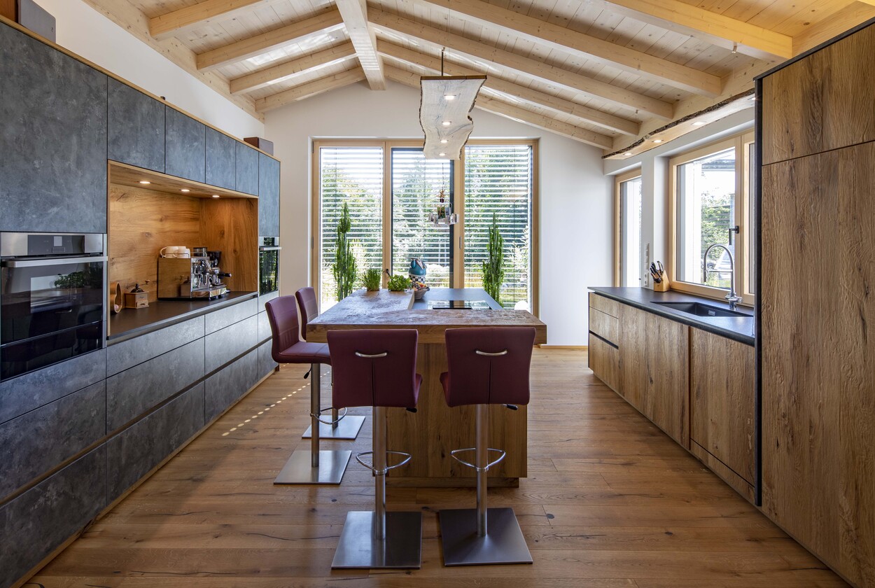 Moderne Küche in einem Einfamilienhaus in Prien mit Holzdekor und großen Fenstern, die viel Tageslicht hereinlassen.