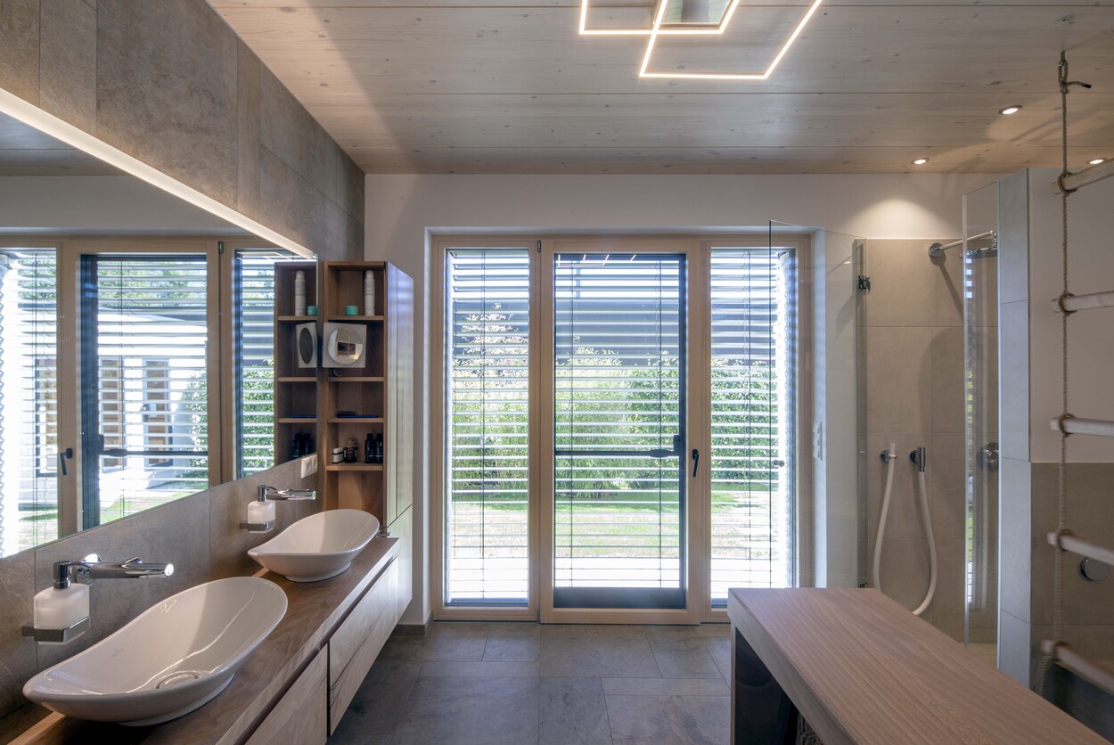 Modernes Badezimmer mit Doppelwaschbecken und großer Dusche bietet einen hellen Blick auf den Garten in einem Einfamilienhaus.