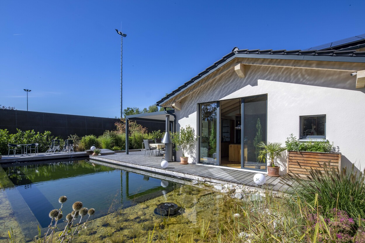 Modernes Einfamilienhaus in Prien mit einer Holzterrasse und einem gepflegten Teich im sonnigen Garten.