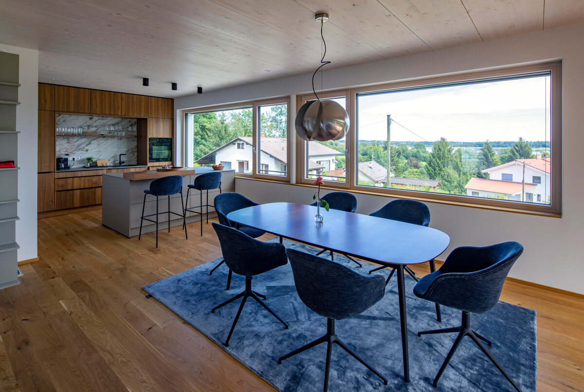 Das Esszimmer im Holzhaus Rimsting zeigt durch große Fenster den weiten Blick auf die grüne Landschaft.