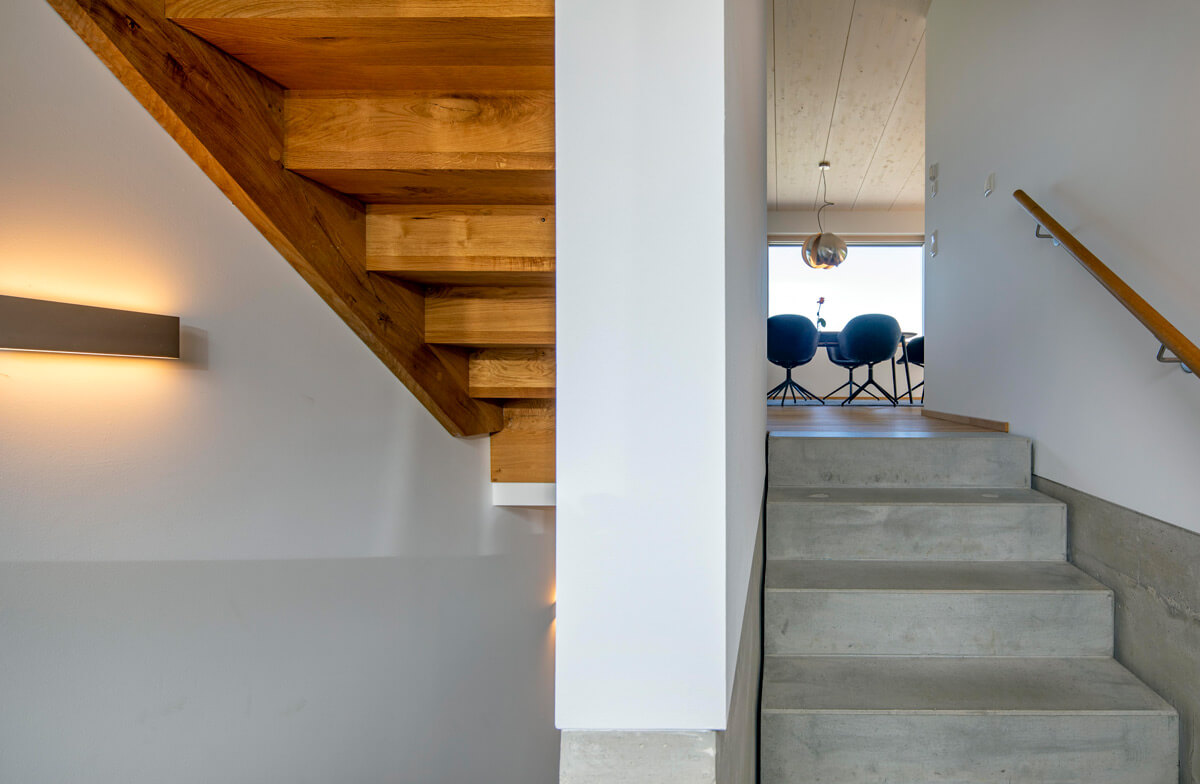 Eine moderne Holztreppe in einem Rimstinger Haus führt zu einem Essbereich mit stilvollen blauen Stühlen.