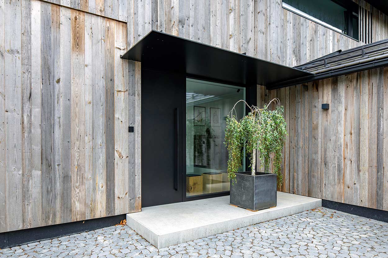 Ein modernes Haus mit Holzverkleidung hat einen schlichten Eingang, der von einem grünen Pflanzkübel betont wird.