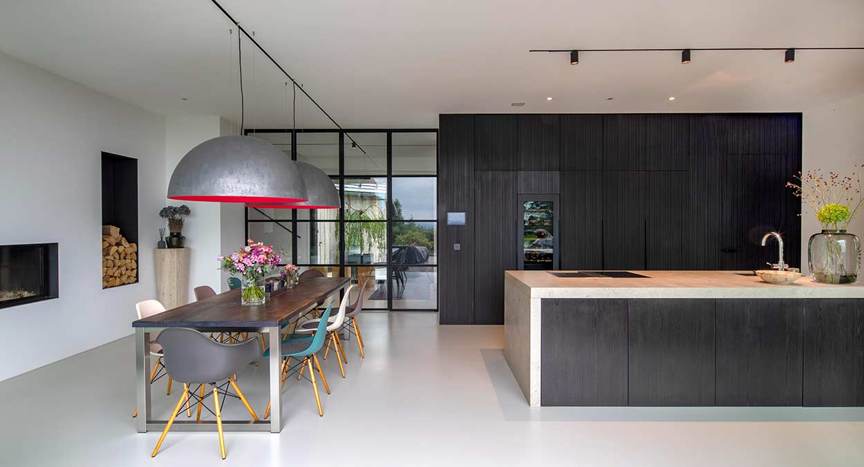 Eine moderne Küche mit großem Esstisch und stilvollen Hängelampen vor einer eleganten dunklen Schrankwand.