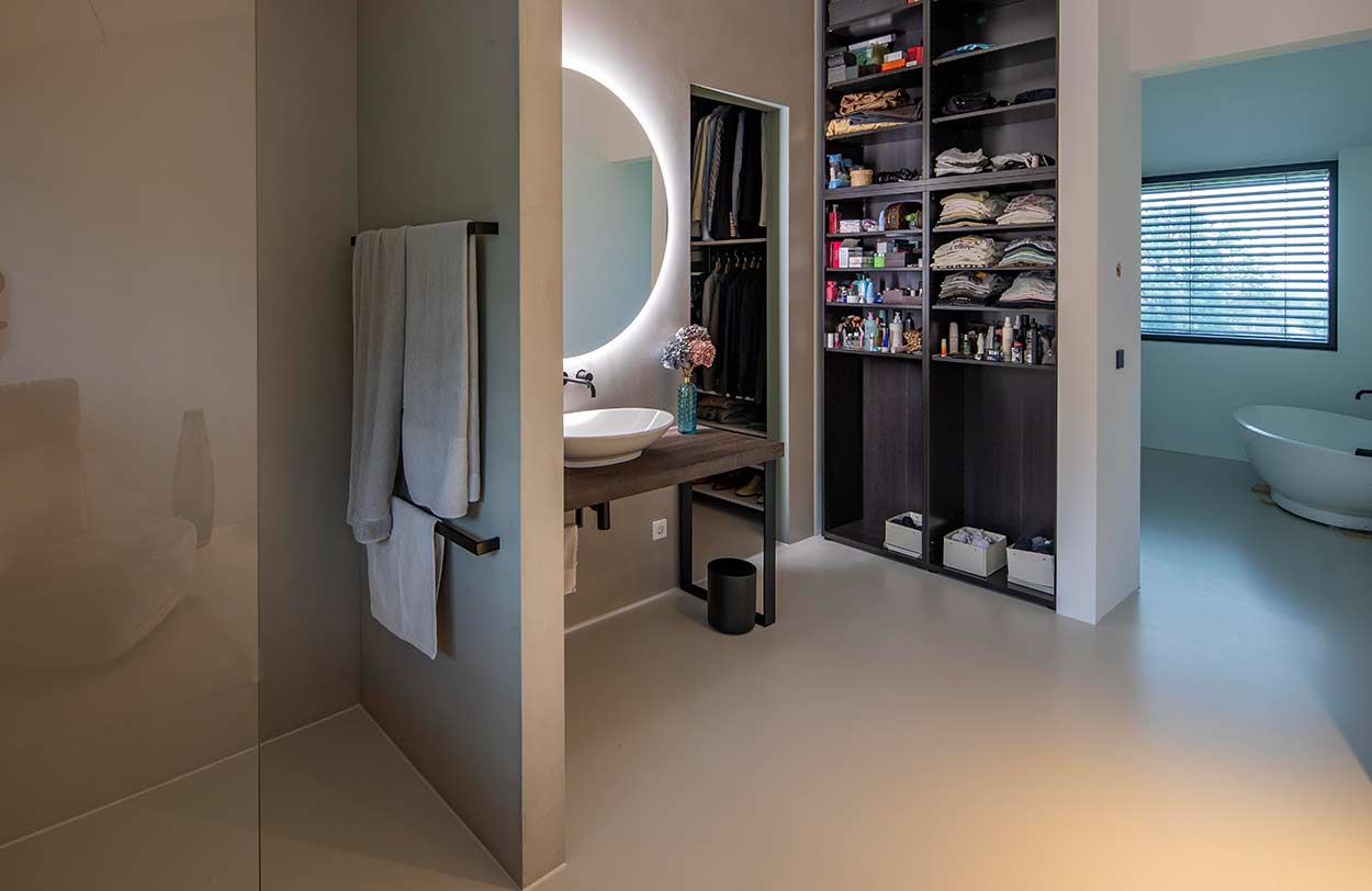 Ein modernes Badezimmer mit großem Spiegel, freistehender Badewanne und offenem Regal voller Kleidung strahlt Eleganz aus.