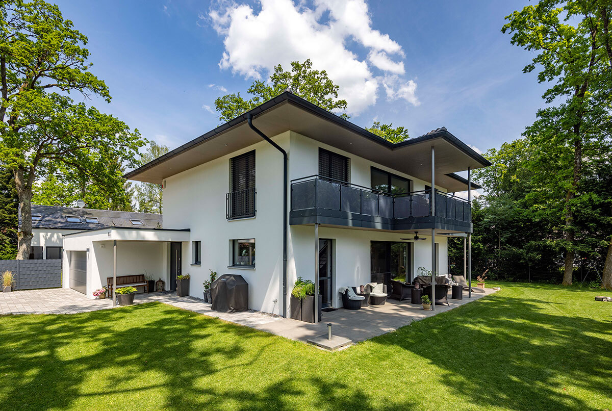 Modernes Energiesparhaus im Münchner Kreis mit großem Garten, Balkon und umgeben von grünen Bäumen unter blauem Himmel.