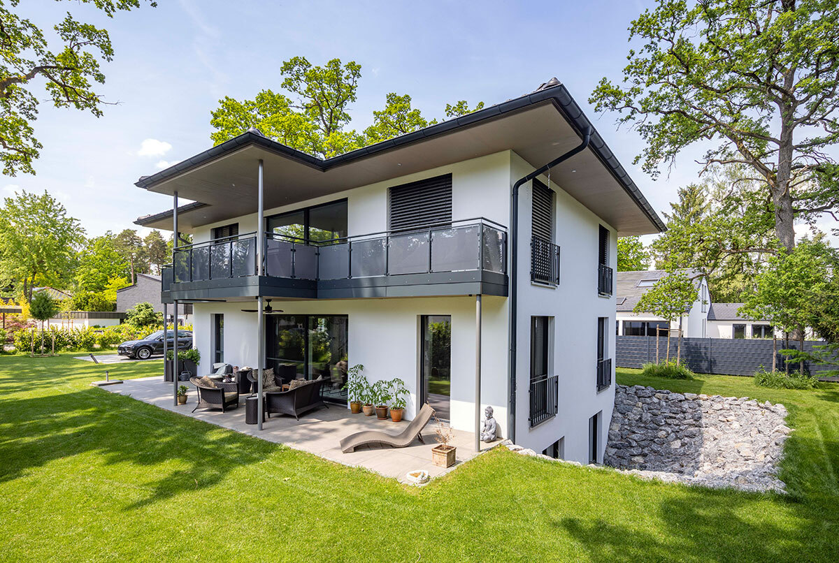Ein modernes Energiesparhaus mit Balkon und Terrasse steht in einem grünen Garten im Kreis München.