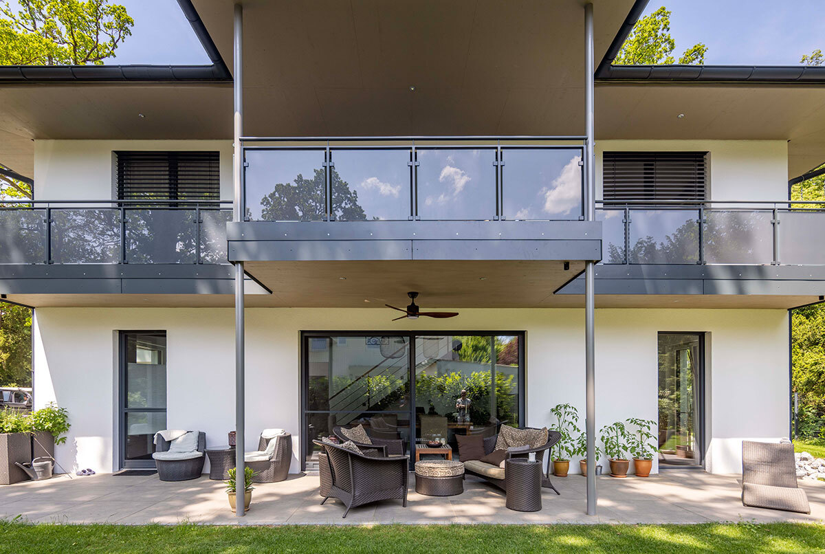 Ein modernes Energiesparhaus im Kreis München mit großzügiger Terrasse und stilvollen Gartenmöbeln strahlt Eleganz aus.