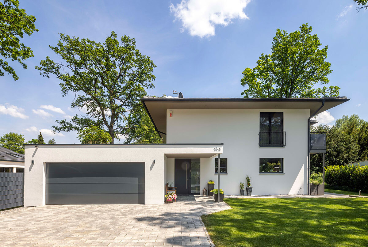 Ein modernes Energiesparhaus im Kreis München mit großzügiger Garage und gepflegtem Garten bei strahlendem Sonnenschein.