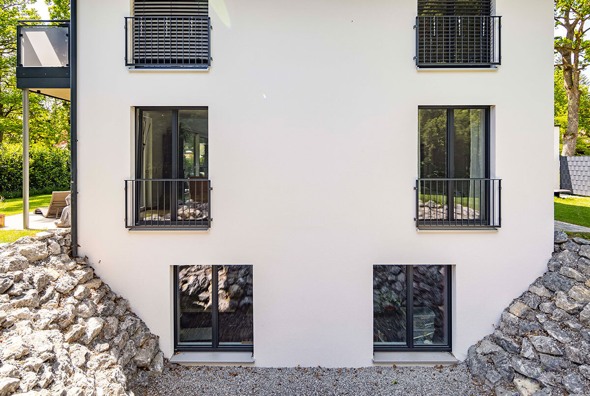 Die Fassade eines modernen Energiesparhauses im Kreis München zeigt große Fenster mit Blick auf einen steinigen Garten.