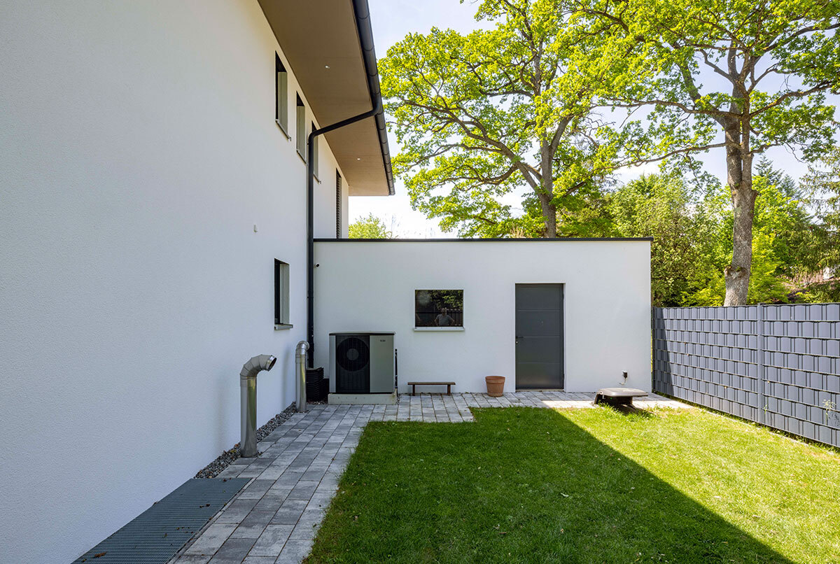 Ein modernes Energiesparhaus im Kreis München mit gepflegtem Garten und hohen, grünen Bäumen im Hintergrund.