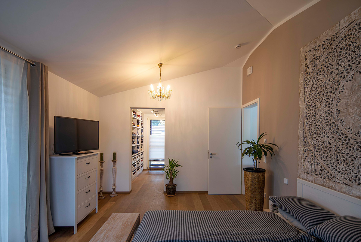 Ein stilvolles Schlafzimmer nahe München mit großem TV, Pflanzen und Blick in den Ankleideraum eines energiesparenden Hauses.