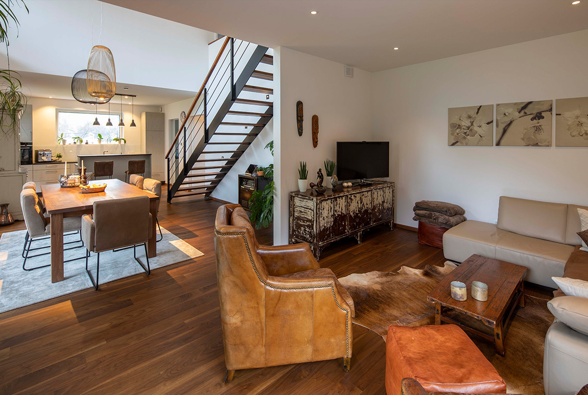 Ein modernes Wohnzimmer im Energiesparhaus bei München zeigt Ledersessel, Holzmöbel und einen einladend offenen Wohnbereich.