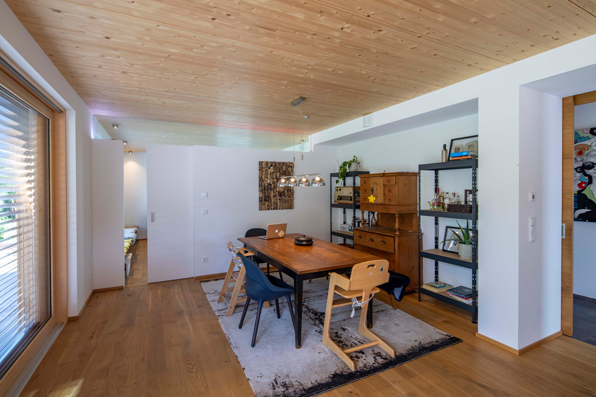 Ein Esszimmer in einem Holzhaus in Neubeuern zeigt einen Holztisch mit modernen Stühlen und Regalen auf hellem Holzboden.