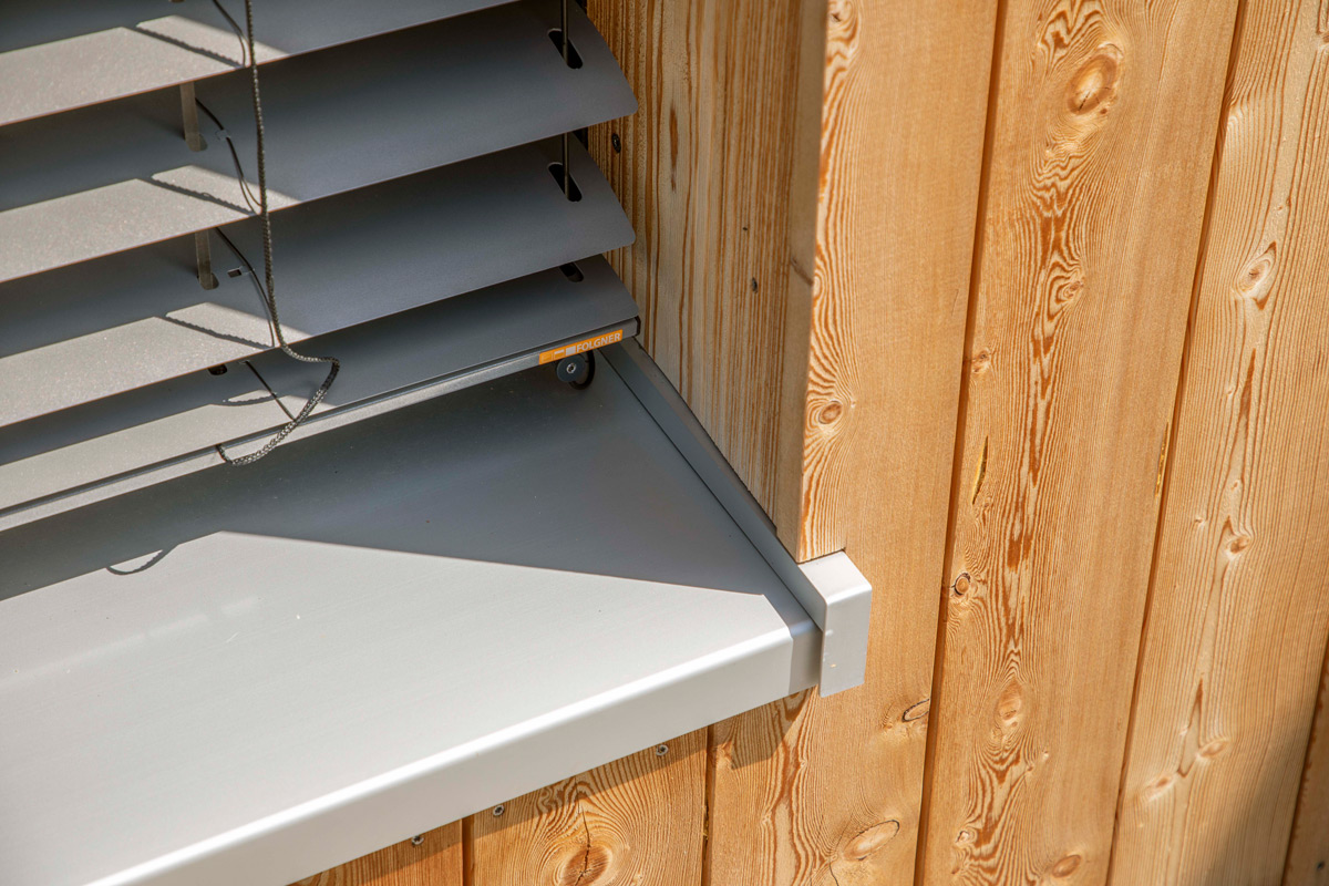 Ein modernes Holzhaus in Neubeuern zeigt ein Fenster mit eleganten Jalousien und einer stilvollen hölzernen Fassade.