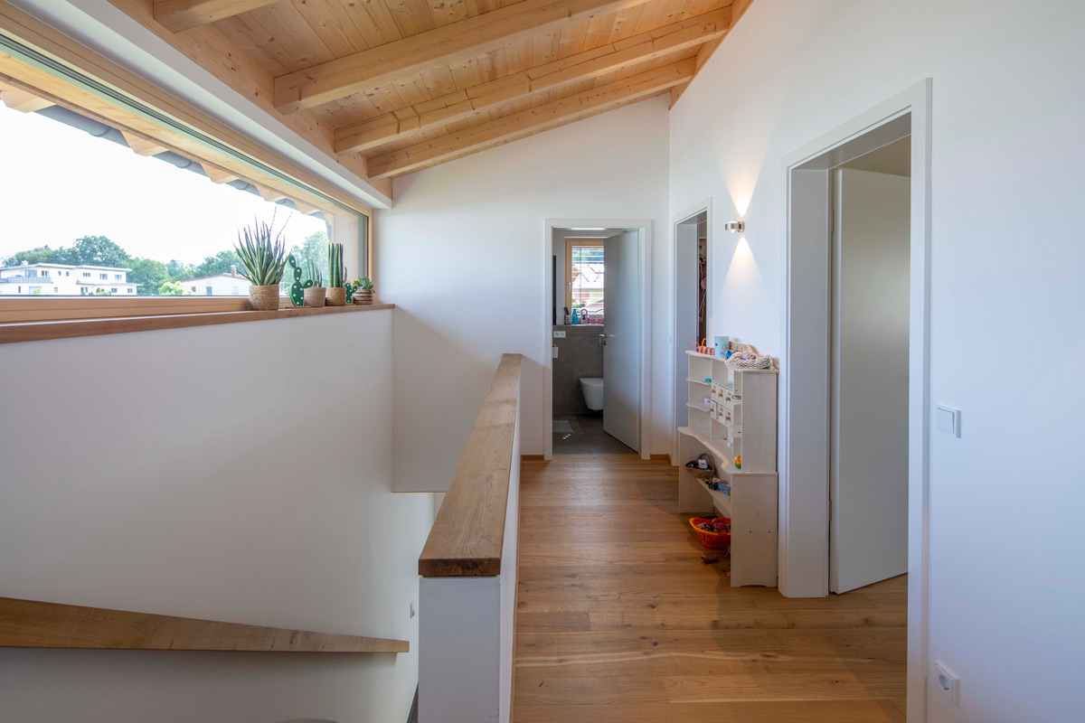 Ein Flur in einem Holzhause in Neubeuern zeigt einen Holzboden und Pflanzen auf der Fensterbank, die Licht einfangen.