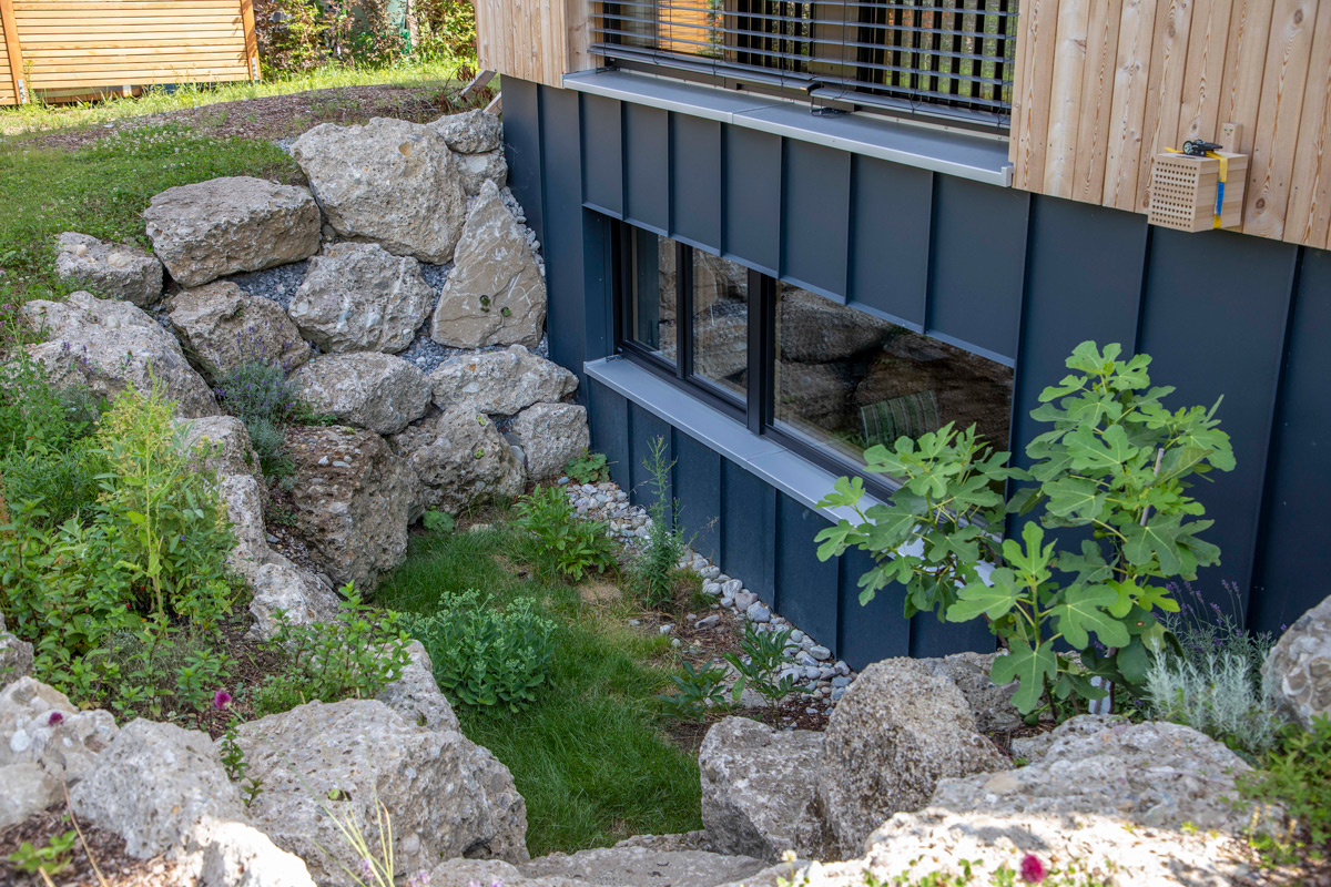 Ein modernes Holzhaus in Neubeuern präsentiert einen gepflegten Garten mit eindrucksvollen Natursteinen und üppigem Grün.