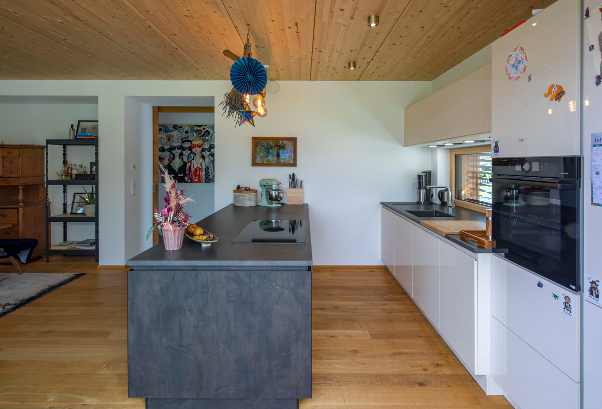 Moderne Küche im Holzhaus von Neubeuern mit Kochinsel, Holzdecke und stilvoller Dekoration für ein elegantes Ambiente.
