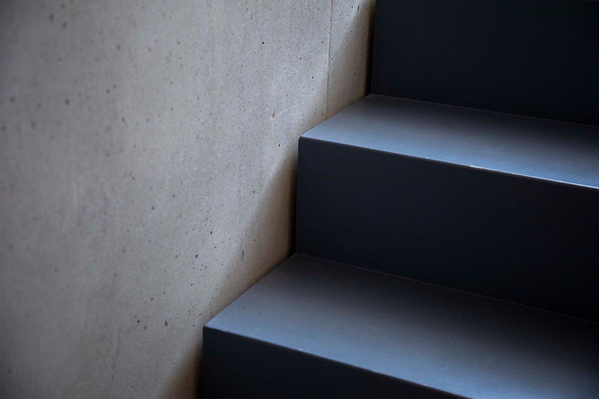 Eine moderne Treppe aus dunklem Holz kontrastiert mit der glatten, grauen Betonwand in einem Haus in Neubeuern.