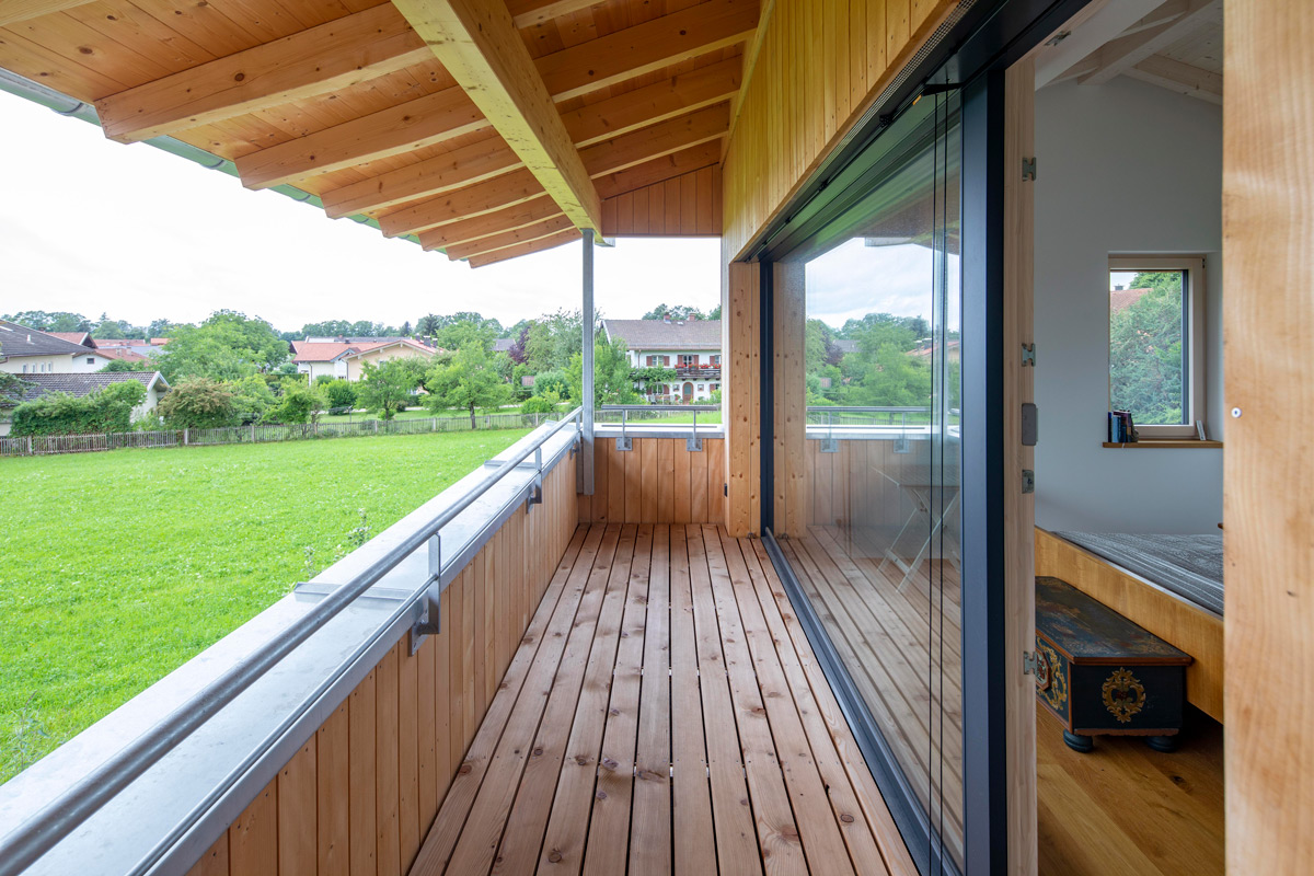 Ein geräumiger Balkon eines Holzhauses in Chieming bietet einen herrlichen Blick auf eine grüne Wiese und benachbarte Häuser.
