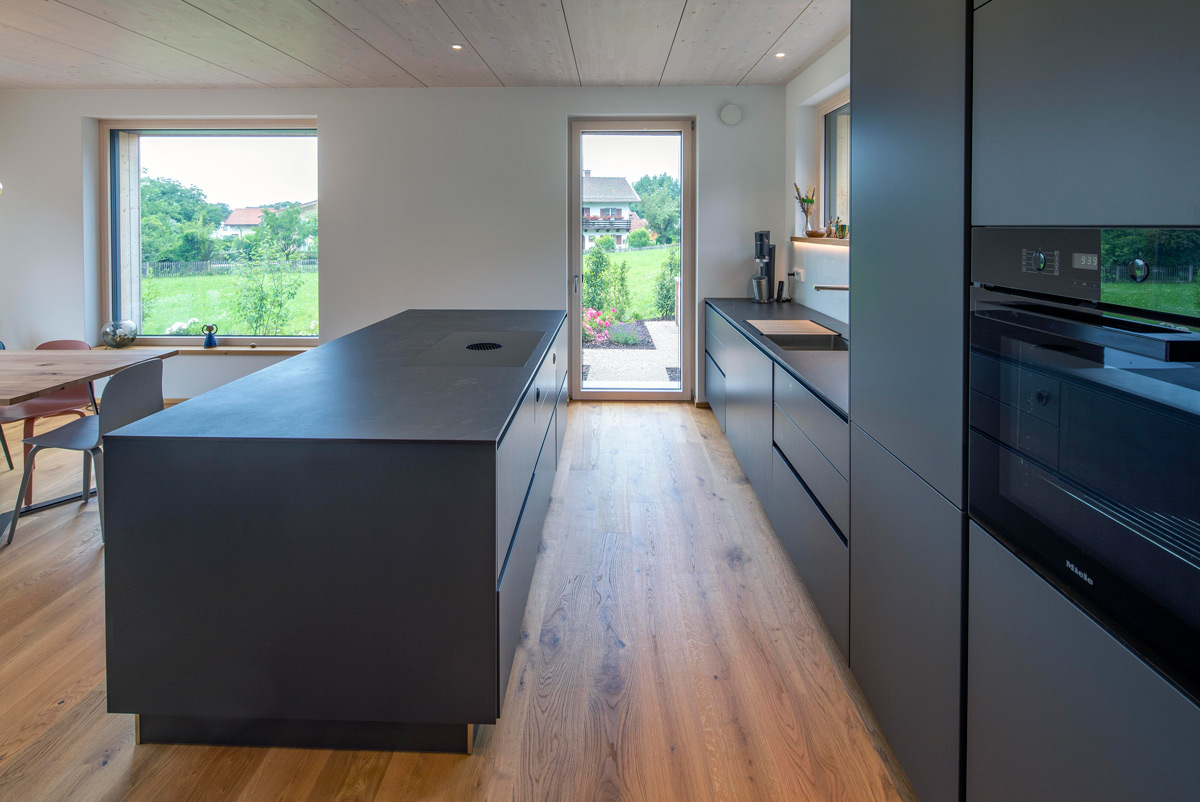 Moderne Küche in einem Holzhaus in Chieming mit grauen Schränken und Blick auf den grünen Garten.