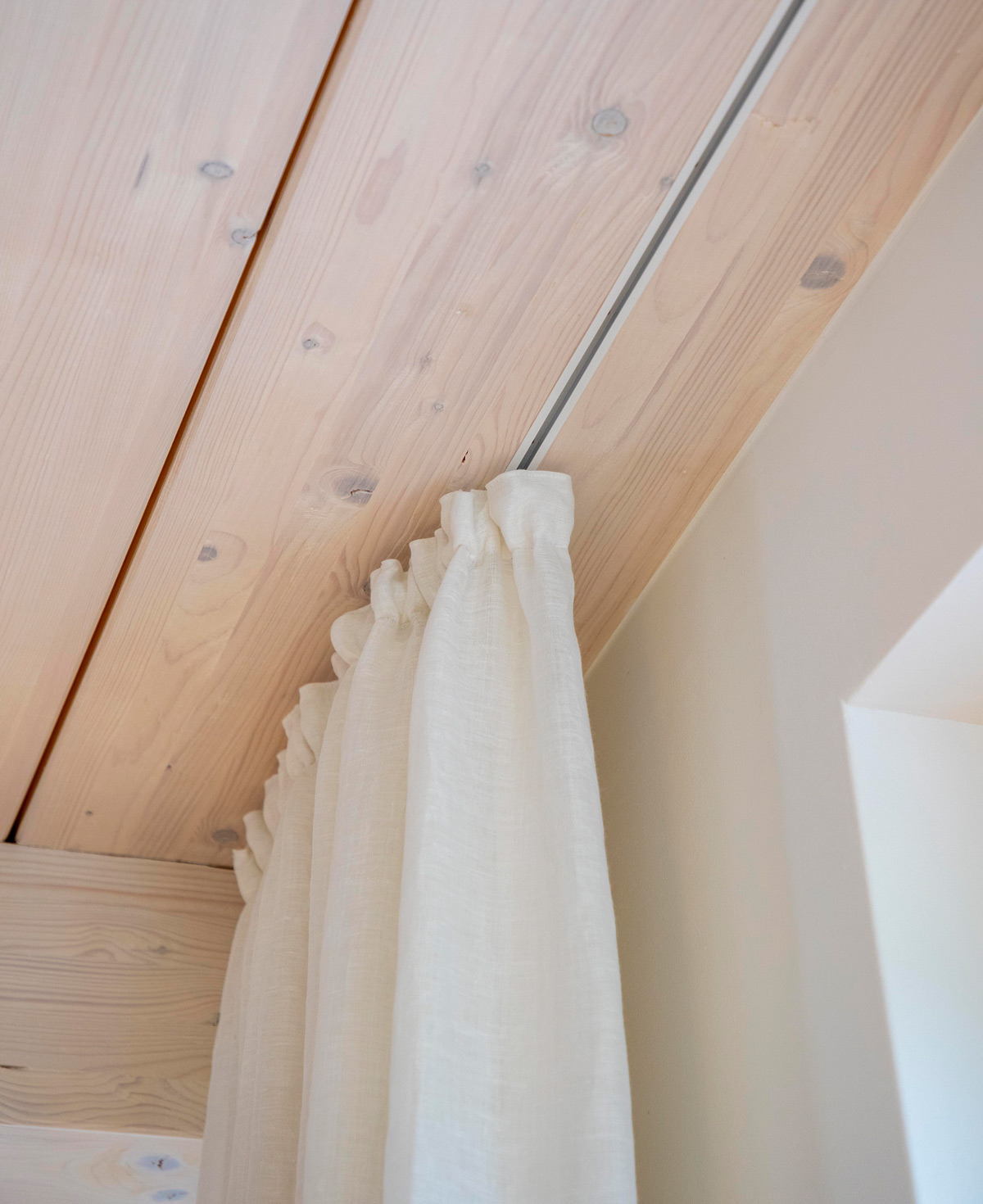 Ein weißer Vorhang hängt an einer Holzdecke in einem Haus in Chieming und schafft eine gemütliche Atmosphäre.