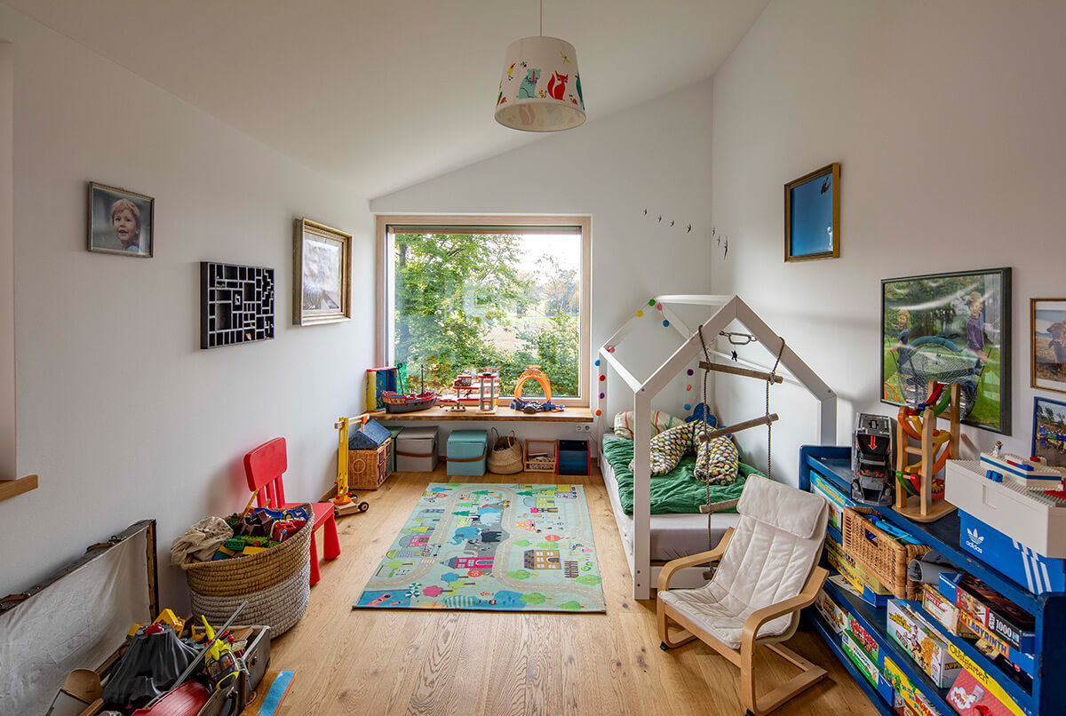 Das helle Kinderzimmer im Holzhaus Oberbiberg ist mit buntem Spielzeug und einem gemütlichen Bett im Hausstil eingerichtet.