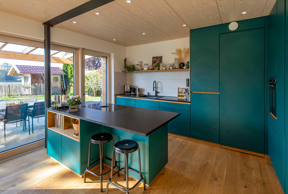 Moderne Küche in einem Holzhaus in Oberbiberg mit grünen Schränken, großer Fensterfront und stilvollem Essbereich.