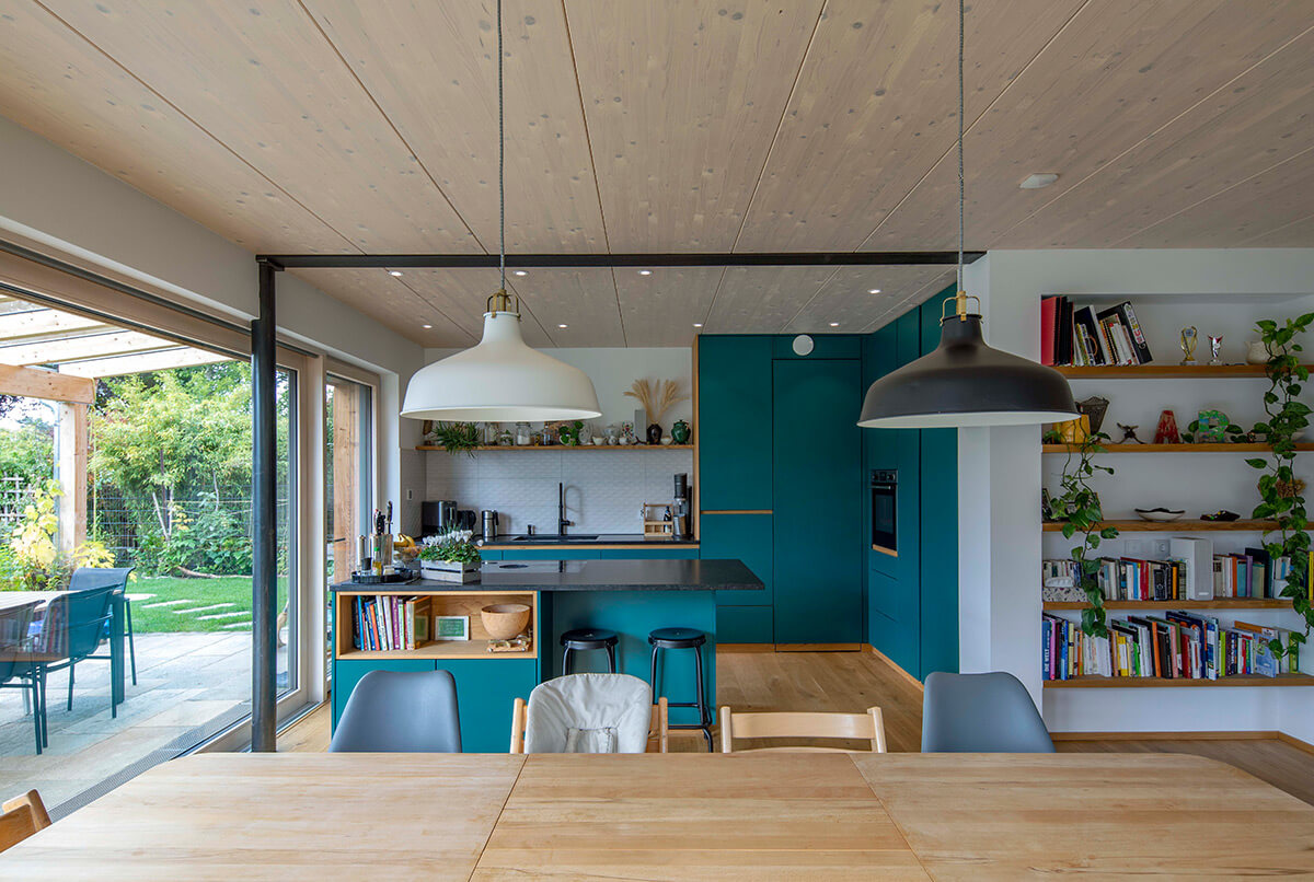 Moderne Holzküche in Oberbiberg mit türkisfarbenen Schränken, Holzregalen und großem Fensterblick auf den grünen Garten.
