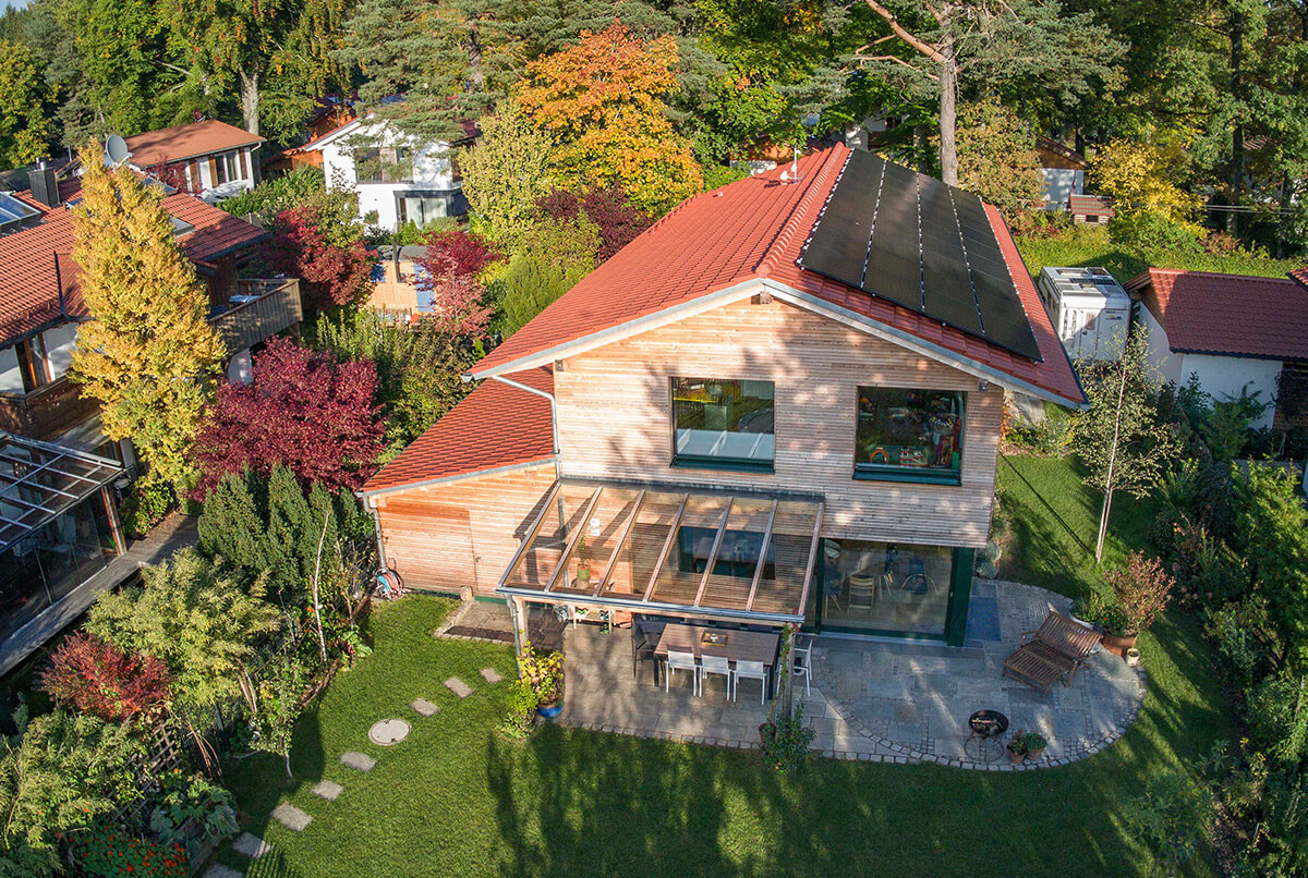 Luftaufnahme eines modernen Holzhauses in Oberbiberg mit Solarpanelen und einem gepflegten Garten in herbstlicher Umgebung.