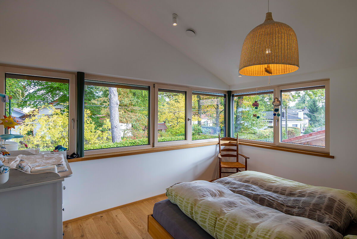 Ein gemütliches Schlafzimmer im Holzhaus Oberbiberg bietet durch große Fenster einen Ausblick auf die grüne Umgebung.