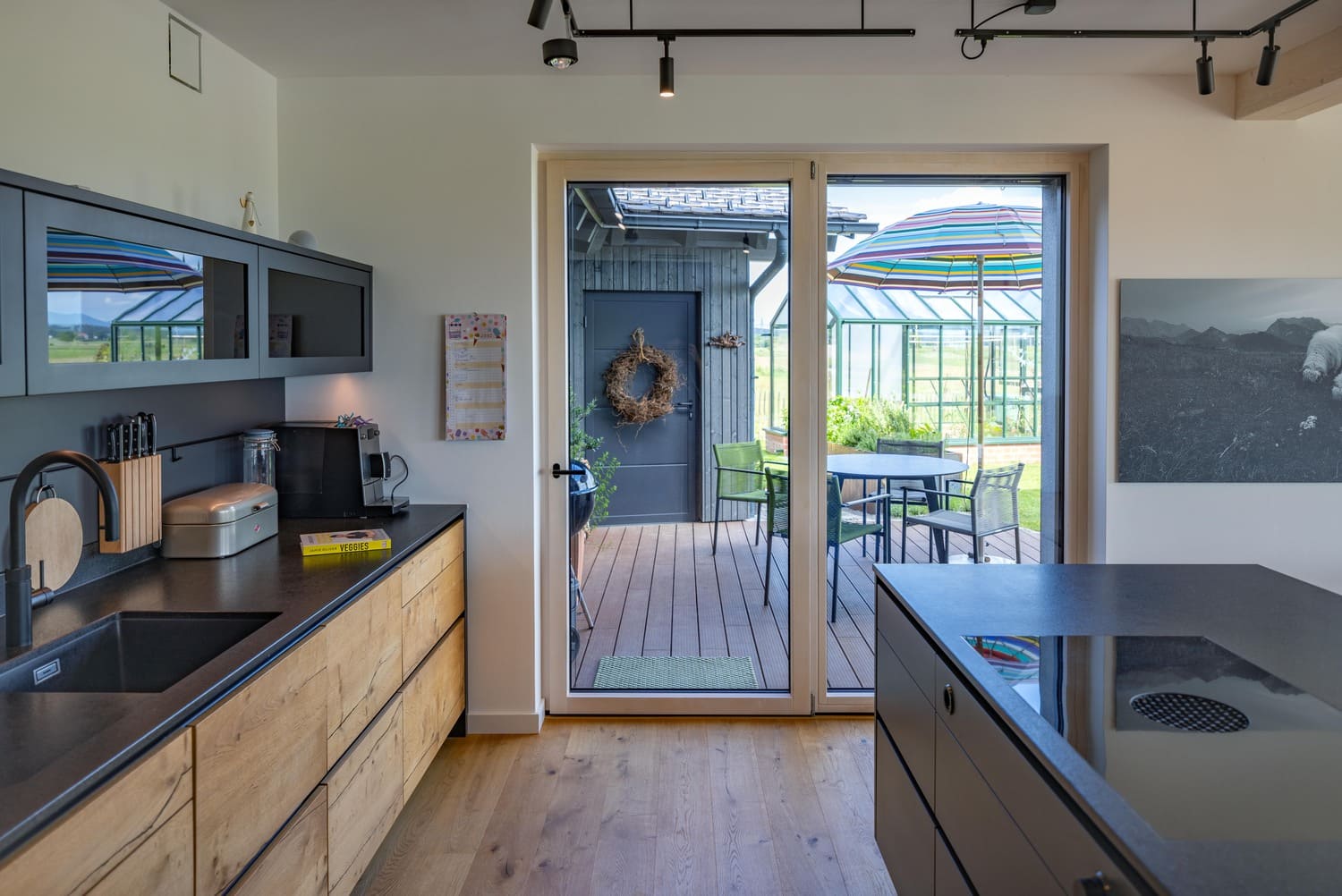 In einer modernen Holzküche in Chieming führen Glastüren auf die Terrasse mit buntem Sonnenschirm und Gartenblick.