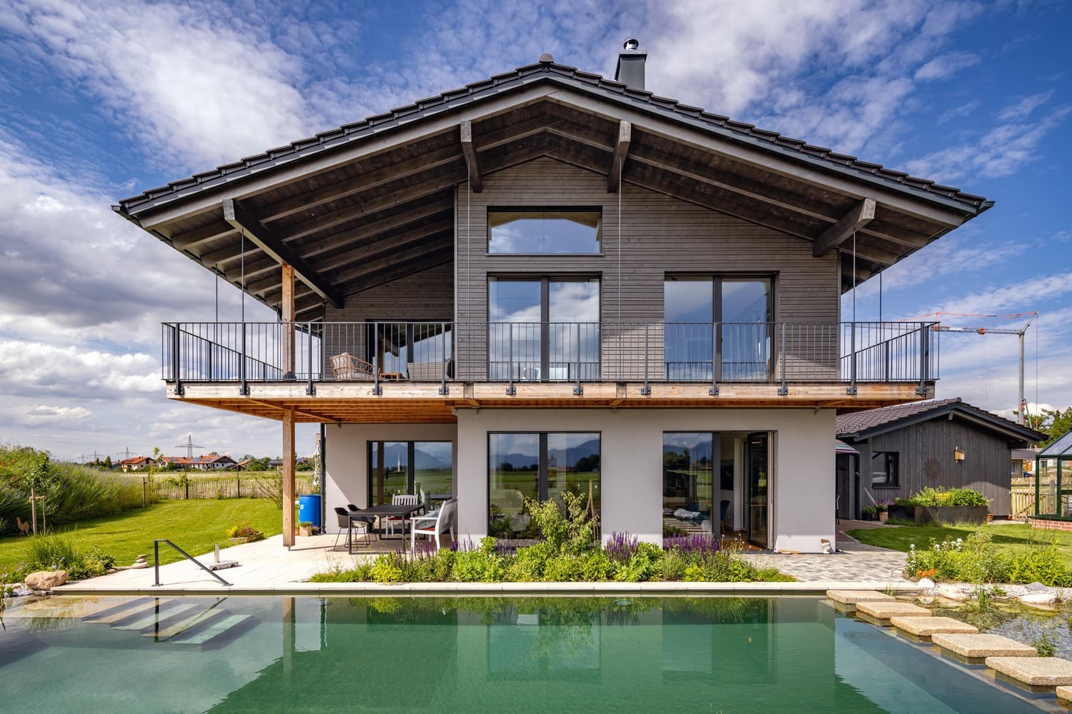 Südansicht Holzhaus Chiemgau mit natur Schwimmteich und Freisitz, bodentiefe Fenster im EG und OG
