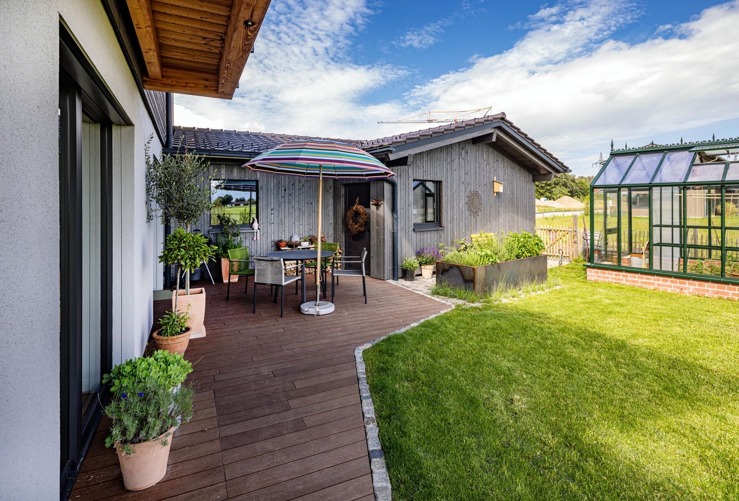 Ostterrasse Holzhaus Chiemgau mit Gewächstaus, graue Holzfassade