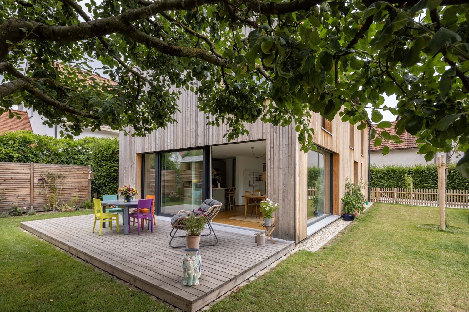 Holzterrasse mit bunten Stühlen, große Glasfenster