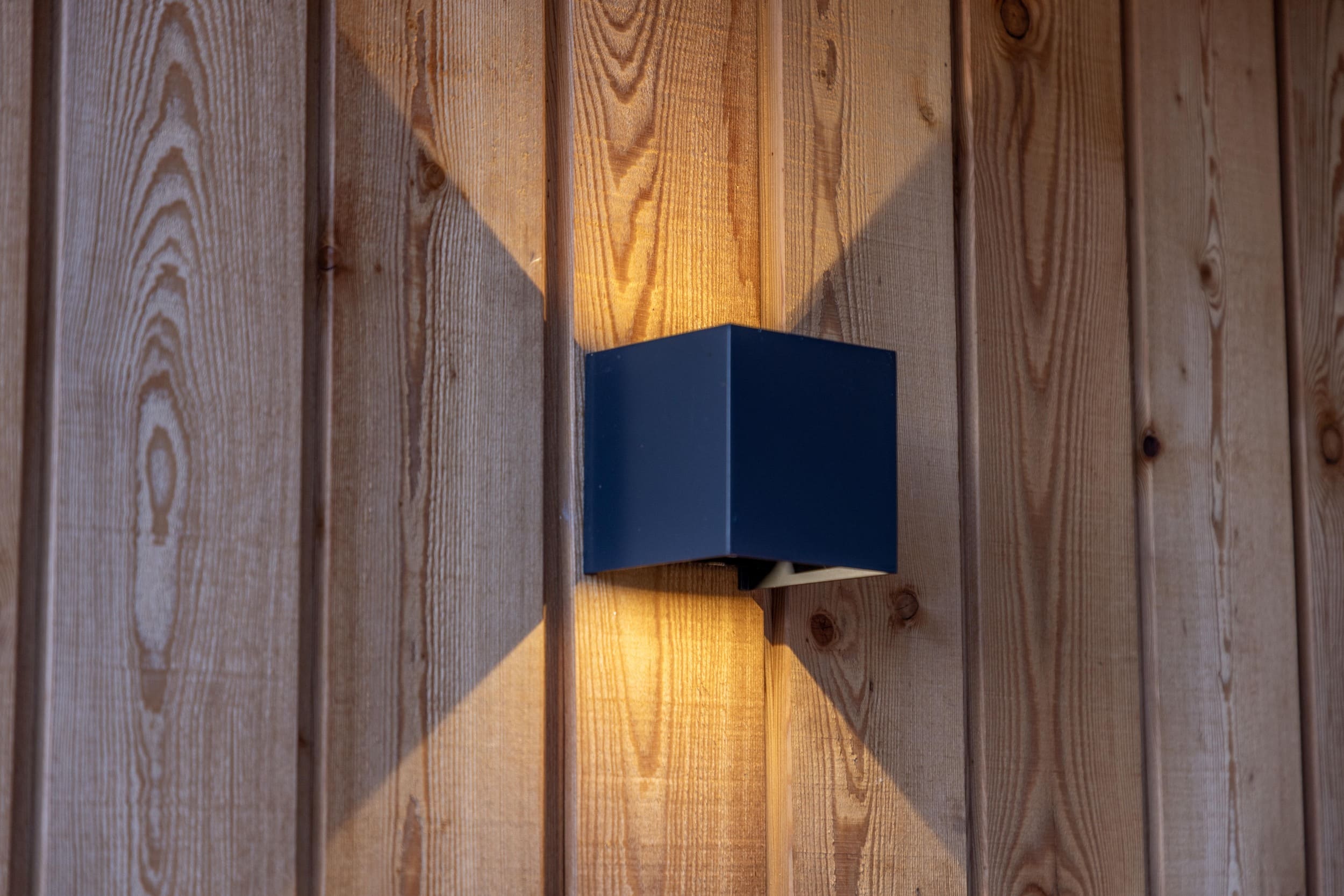 Eine Wandleuchte wirft ein sanftes Lichtmuster auf die vertäfelte Holzoberfläche, die im warmen Glanz erstrahlt.