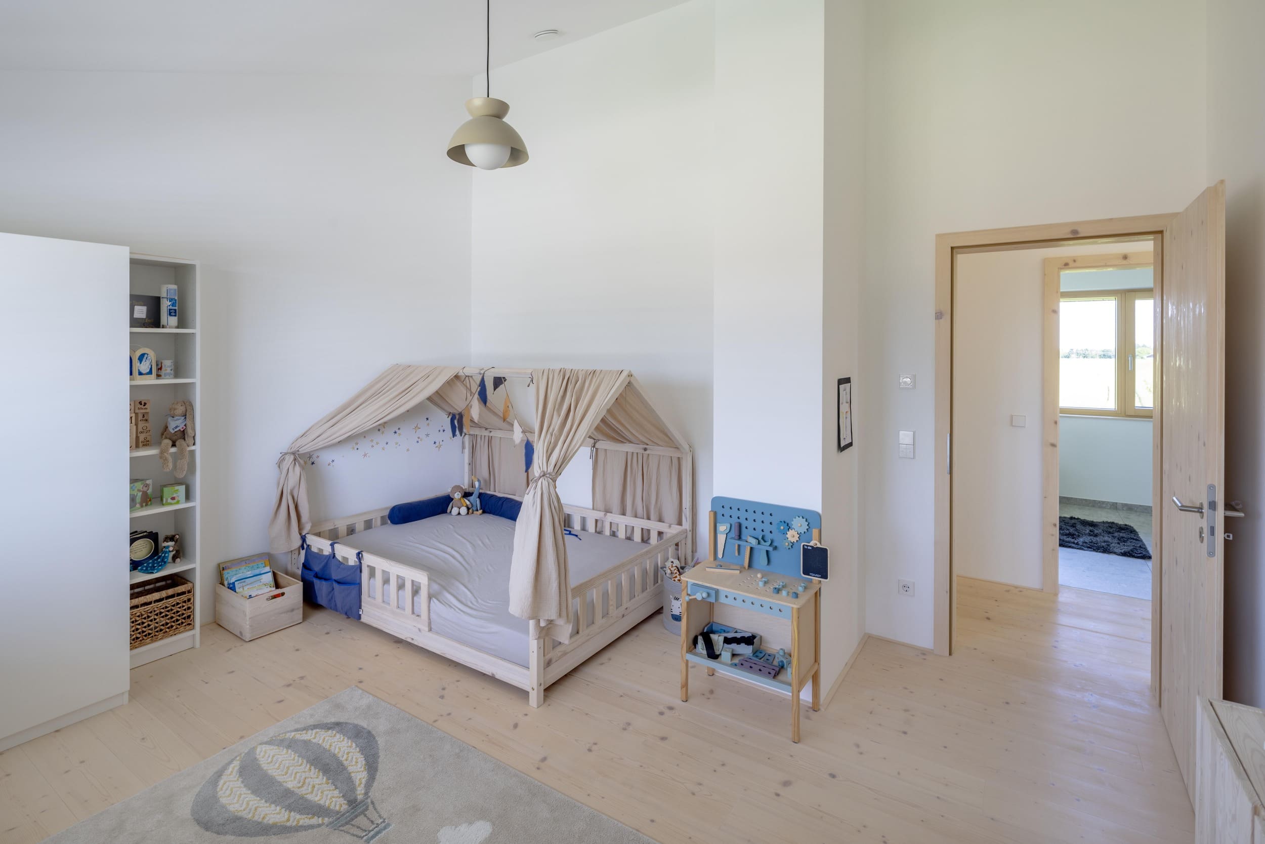 Ein stilvoll eingerichtetes Kinderzimmer mit einem hölzernen Baldachinbett und einem Spielzeugregal in heller Umgebung.