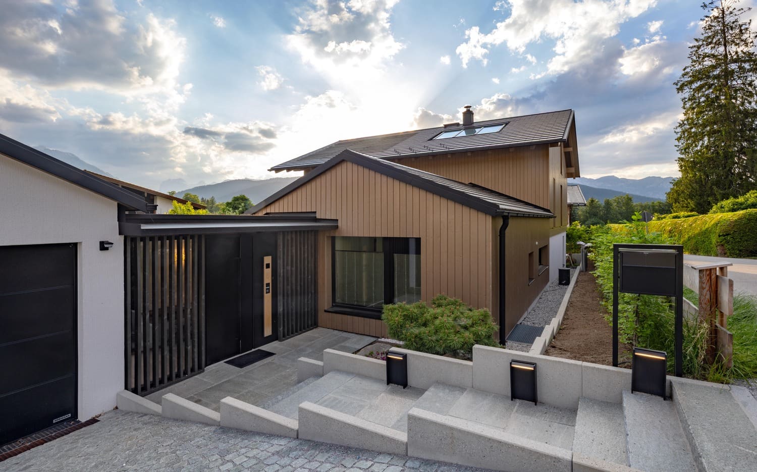 Moderne Architektur eines Hauses mit Strukturen aus Holz und Stein, umgeben von Natur und unter einem sonnigen Himmel.