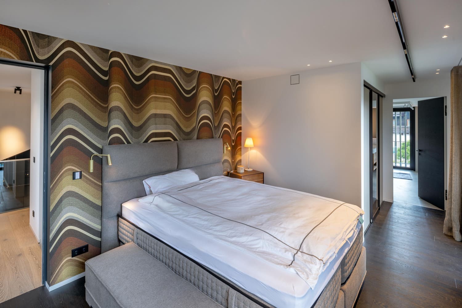 Elegantes Schlafzimmer mit Wellenmuster-Tapete, einem Bett und einer gemütlichen Lampe. | © Name