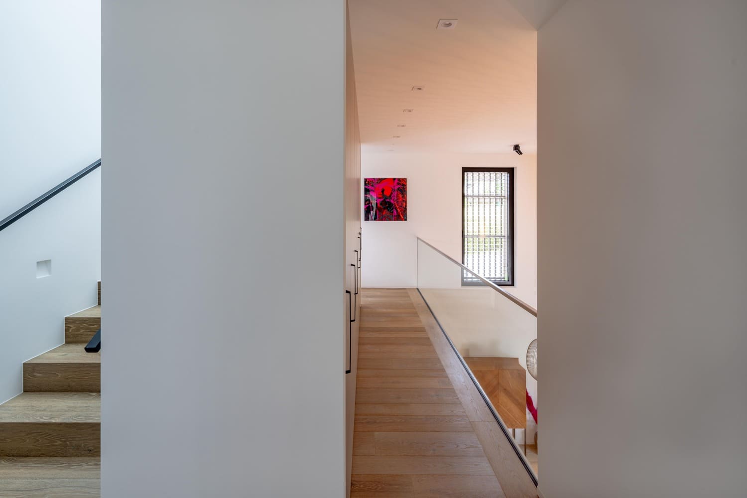 Ein heller Flur mit Holztreppe und modernem Kunstwerk an der Wand, das einladend wirkt. | © Name