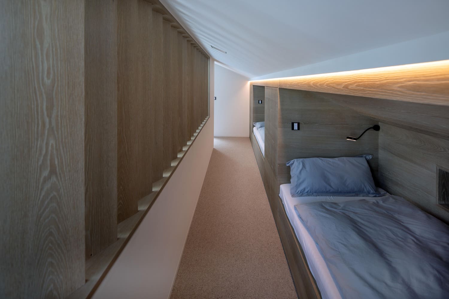 Ein moderner Schlafbereich mit Holzverkleidung und zwei Betten in einem hellen Raum. | © Name