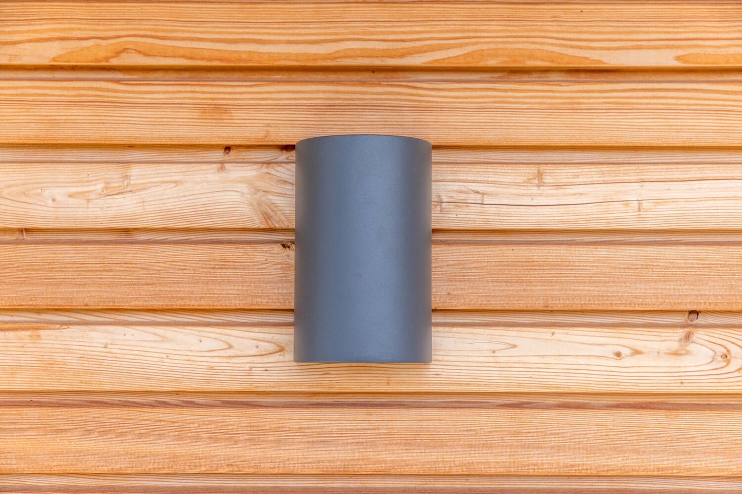 Eine graue Wandlampe ist stilvoll an einer hellen Holzverkleidung montiert.